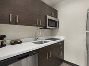 Bright studio suite kitchen featuring full-size refrigerator, stovetop, microwave, and dishwasher.