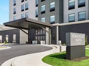 Modern Homewood Suites hotel exterior featuring monument sign, lush green grass, and covered entrance.