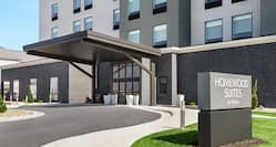 Modern Homewood Suites hotel exterior featuring monument sign, lush green grass, and covered entrance.