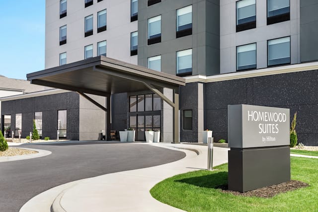 Modern Homewood Suites hotel exterior featuring monument sign, lush green grass, and covered entrance.