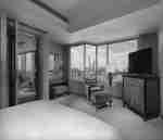 Спальня с одной большой кроватью King Size, креслом, подставкой для ног, HD-телевизором и видом на город