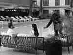 Man and woman relaxing on poolside seating while staff member serves drink