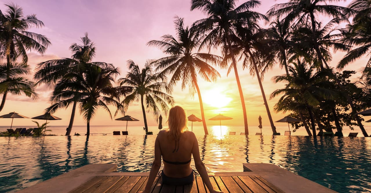  Woman relaxing by the pool in a luxurious beachfront hotel resort at sunset enjoying perfect beach holiday vacation