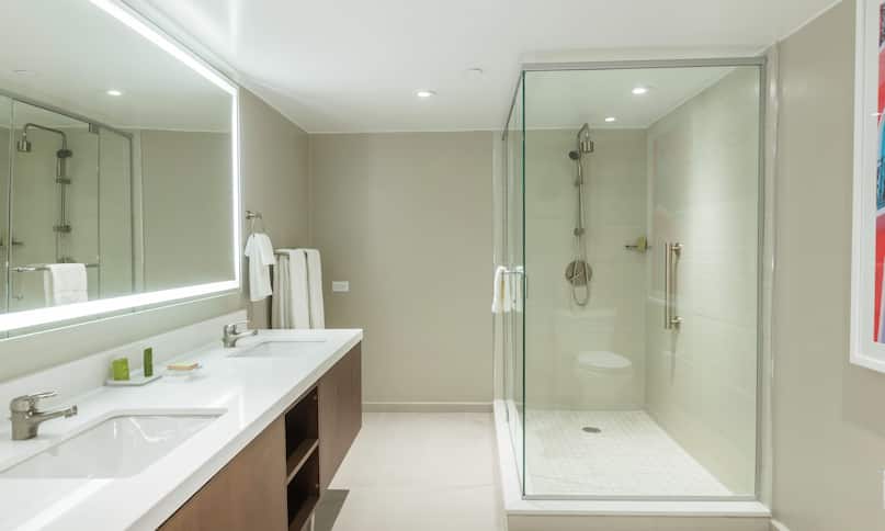 Baño con área de tocador con dos lavamanos y ducha con puerta de vidrio, transición anterior