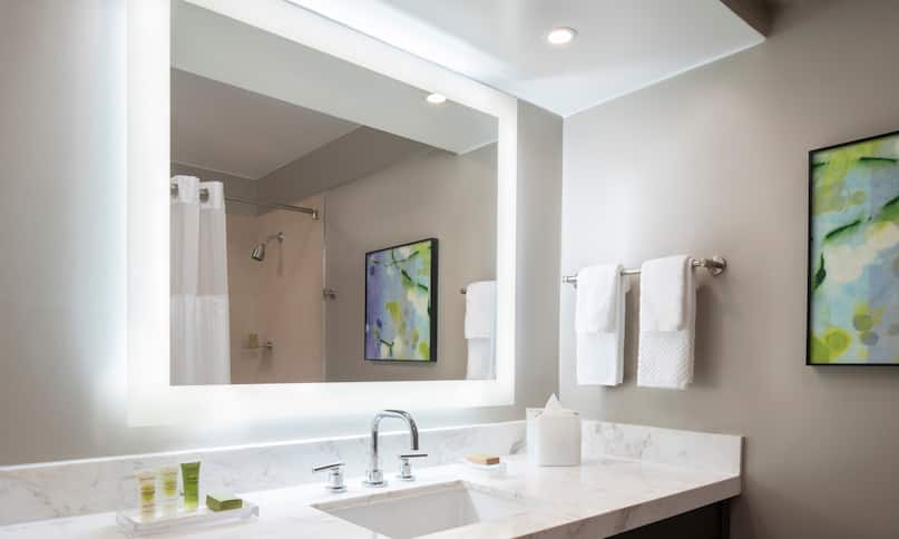 Área de tocador del baño con espejo iluminado, transición anterior
