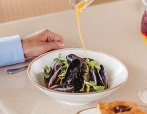 a person pouring sauce on a plate of mussels at The Garden Restaurant