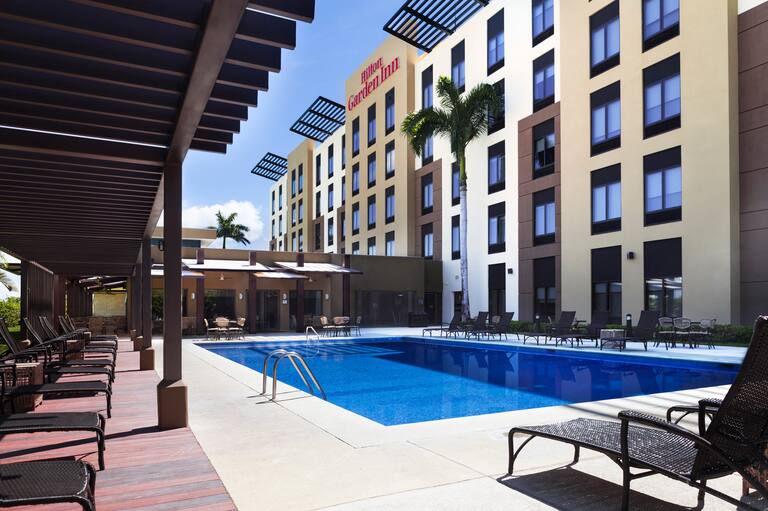 Outdoor Pool with Chaise Lounge Chairs and View of Hotel Exterior and Signage on a Sunny Day