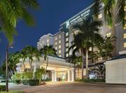 Beautiful Embassy Suites hotel exterior featuring a porte cochere, glowing guestroom windows, and tropical palm trees.