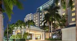 Beautiful Embassy Suites hotel exterior featuring a porte cochere, glowing guestroom windows, and tropical palm trees.