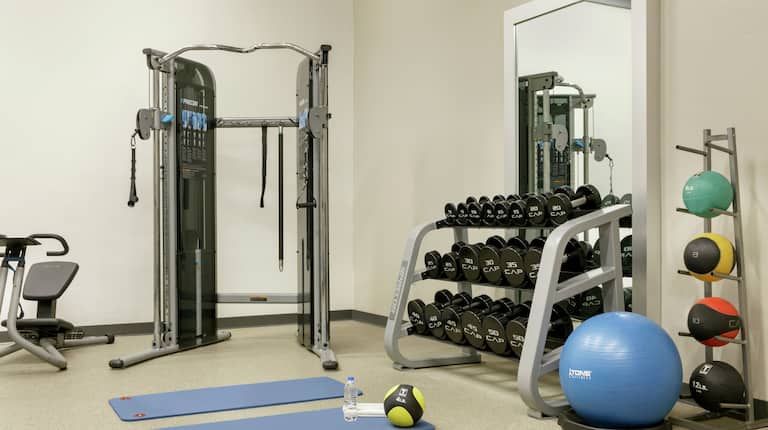 Conveniente gimnasio en el hotel con máquinas para hacer ejercicio, juegos de pesas y colchonetas de yoga.