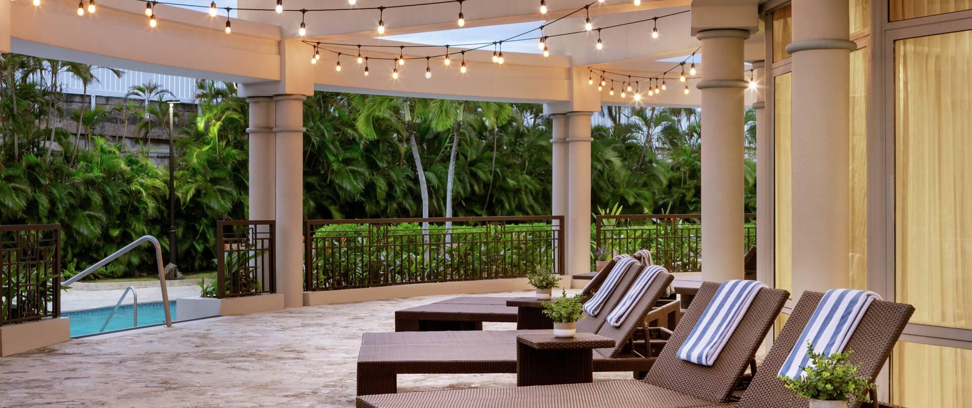 Spacieuse terrasse de la piscine La Vista avec des chaises longues, des serviettes et des lumières suspendues.