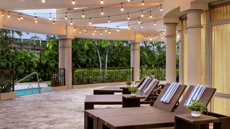 Amplia terraza de la piscina La Vista con divanes, toallas y hermosas cuerdas de luces.