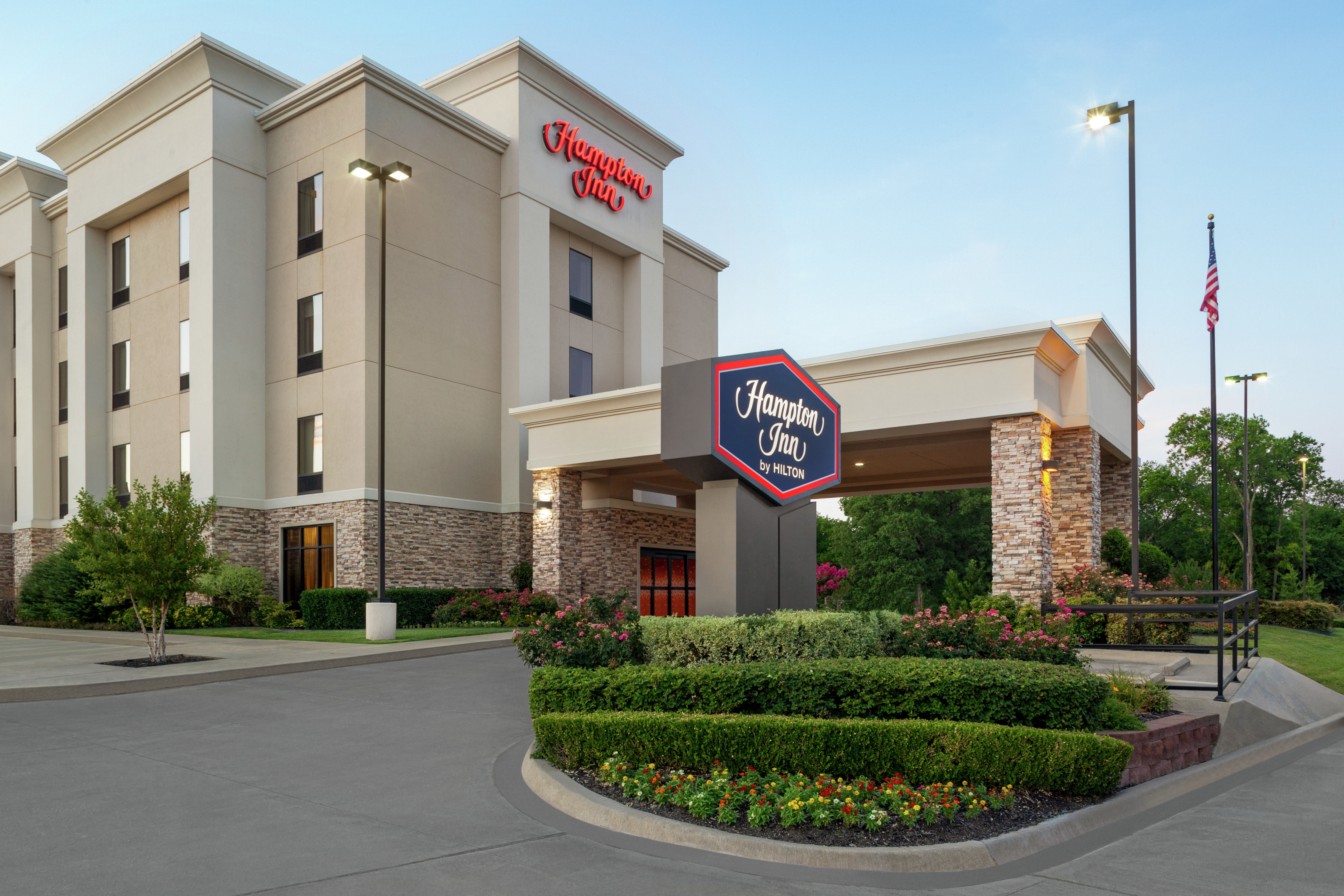 Welcoming Hampton Inn hotel exterior featuring lush landscaping, porte cochere, and dusk sky.