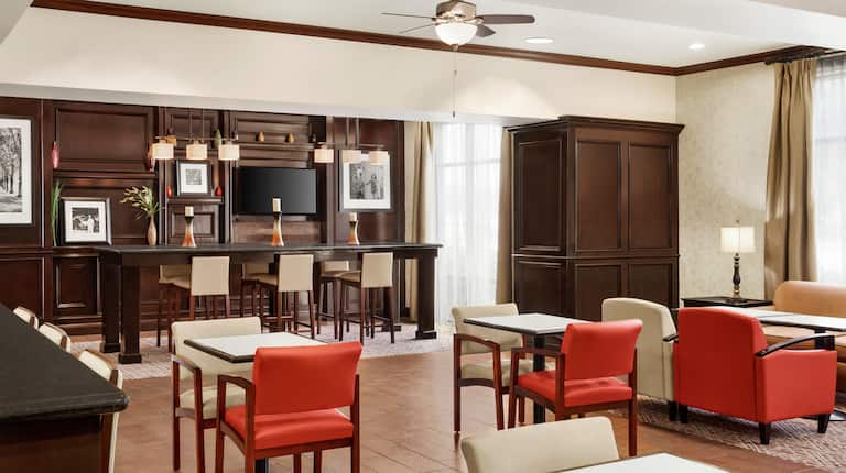 Bright hotel lobby featuring ample seating for guests, large communal table, and TV.