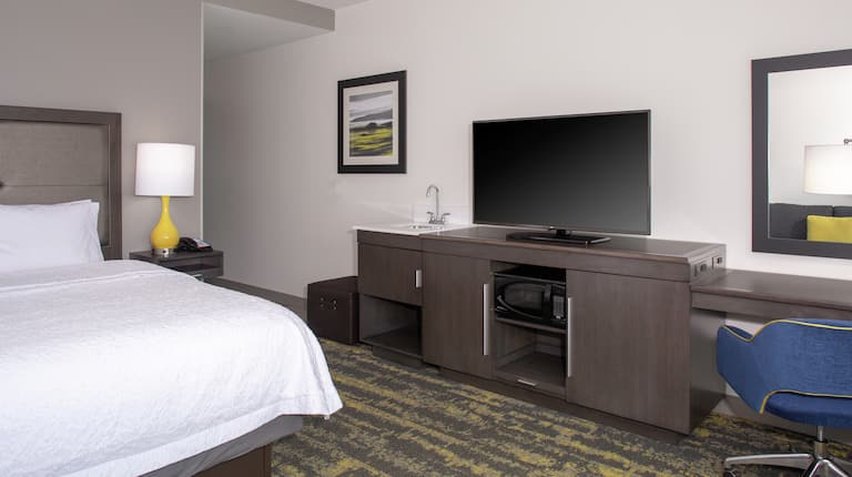 King Bed with TV Sitting on Cabinet Holding the Microwave and Mini Fridge