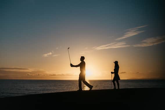 a couple playing golf next to a beach at sunset