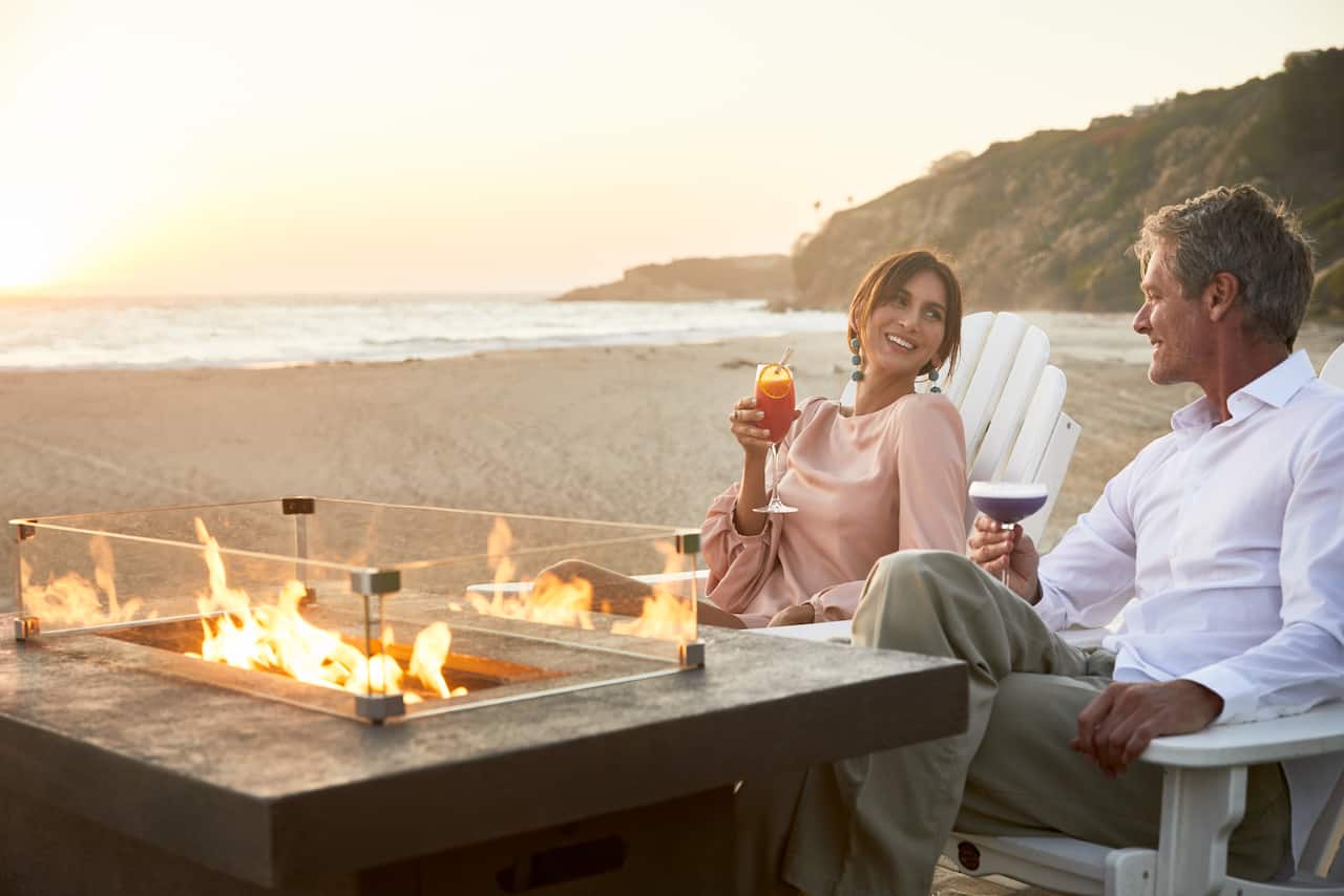 Couple Enjoying Drinks on a Table with a Fire Pit at the Beach