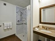 Fresh Towels, Roll-In Shower With Grab Bars and Handheld Showerhead, Vanity Mirror, Sink, and Toiletries in Accessible Bathroom