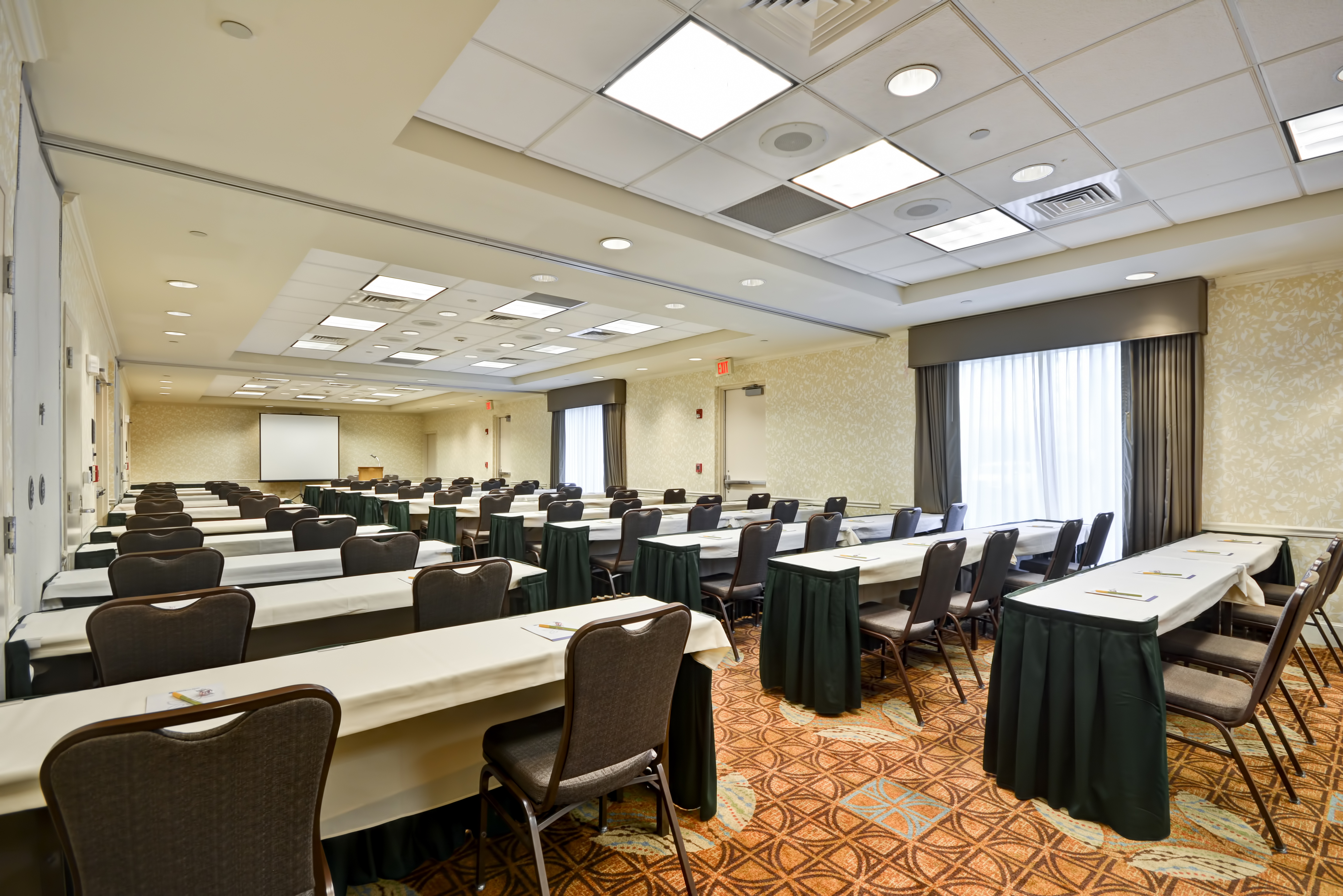 Classroom Setup in Meeting Room With Tables and Chairs Facing Presentation Screen and Podium