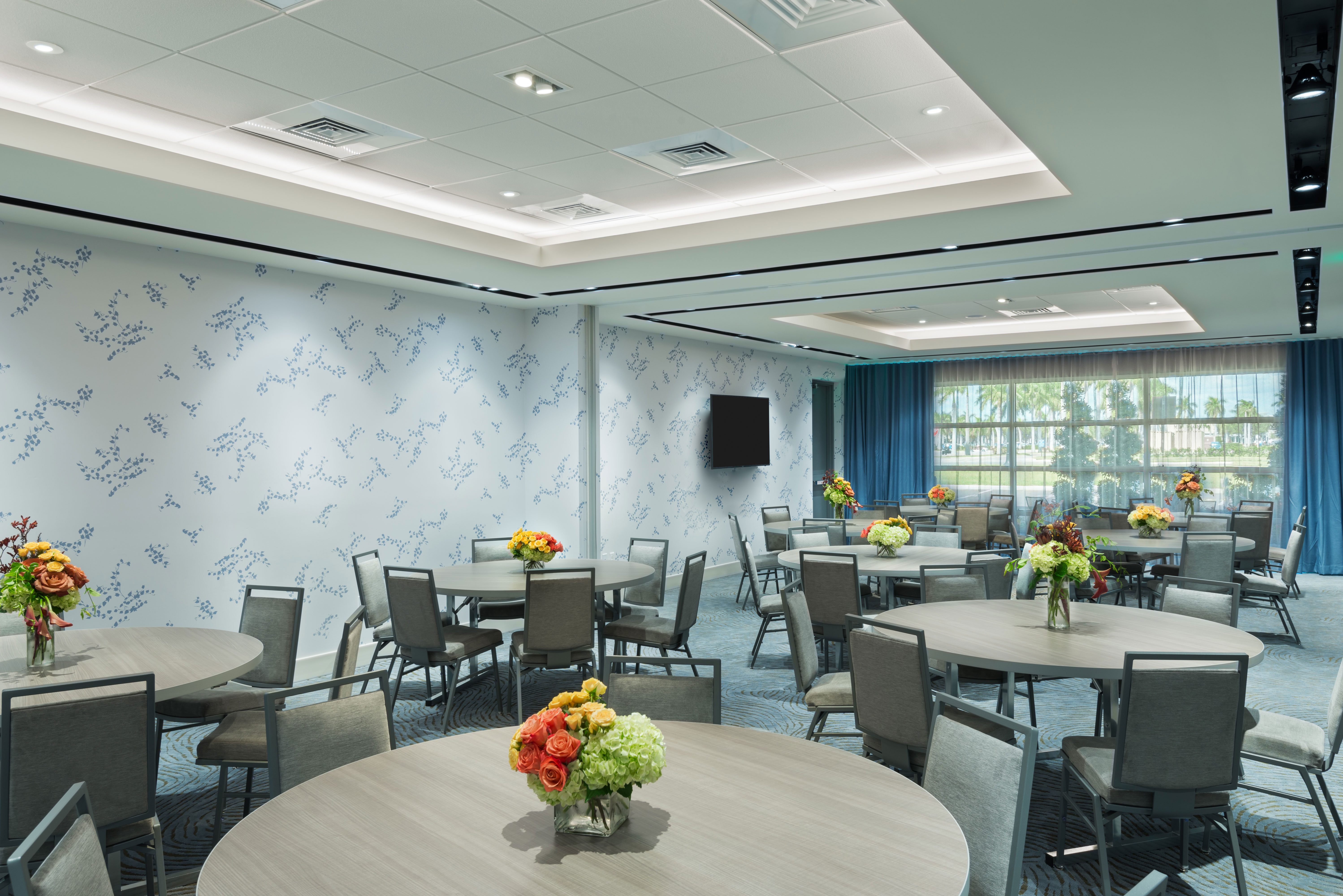 Meeting Room With TV, Seating at Round Tables with Floral Centerpieces, and an Outside View