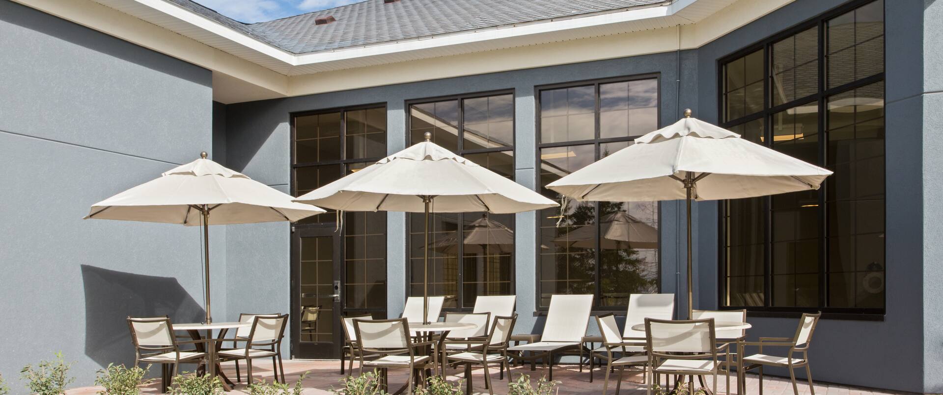 Tables With Umbrellas, Chairs, Landscaping, and Hotel Exterior