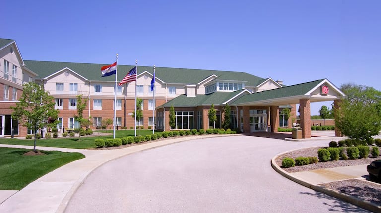 Daytime View of Hotel Exterior, Flagpoles, Landscaping, and Porte Cochère