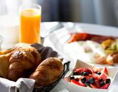 Close up of a bowl of berries, a basket of pastries, and a glass of orange juice