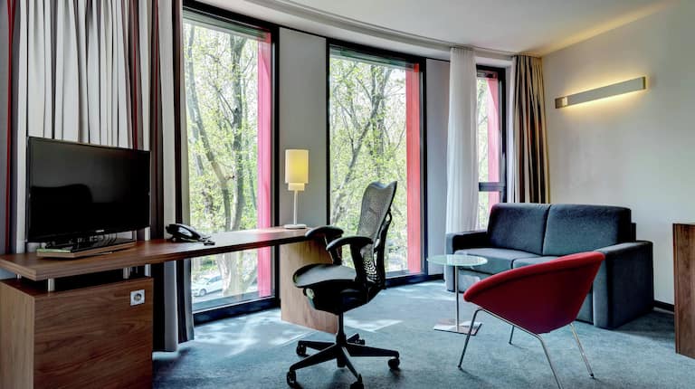 Geräumiges Deluxe Zimmer mit Fernseher, Schreibtisch und Sofa am großen Fenster