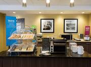 Breakfast serving area with coffee, juice, cereals, oatmeal, pastries, waffle station, and dining amenities