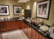 Breakfast serving area with buffet tray, coffee, juice, cereals, oatmeal, pastries, and dining amenities