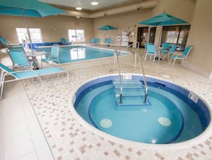 Indoor Pool and jacuzzi with lounge chairs, umbrella covers, and windows with outdoor view
