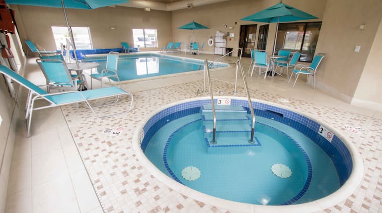 Indoor Pool and jacuzzi with lounge chairs, umbrella covers, and windows with outdoor view