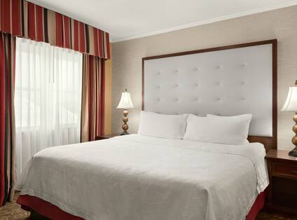 Bright bedroom in suite with comfortable king bed, lamps, and luxurious upholstered headboard. 