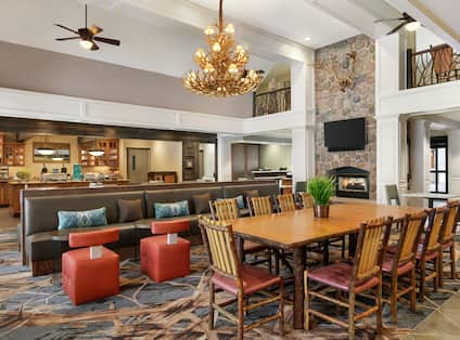 Spacious lodge area with rustic atmosphere featuring communal tables, chairs, fireplace, TV, and breakfast buffet.
