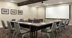 Spacious meeting room with u shape seating arrangement, notepads, pens, citrus water and large projector screen at front of room.