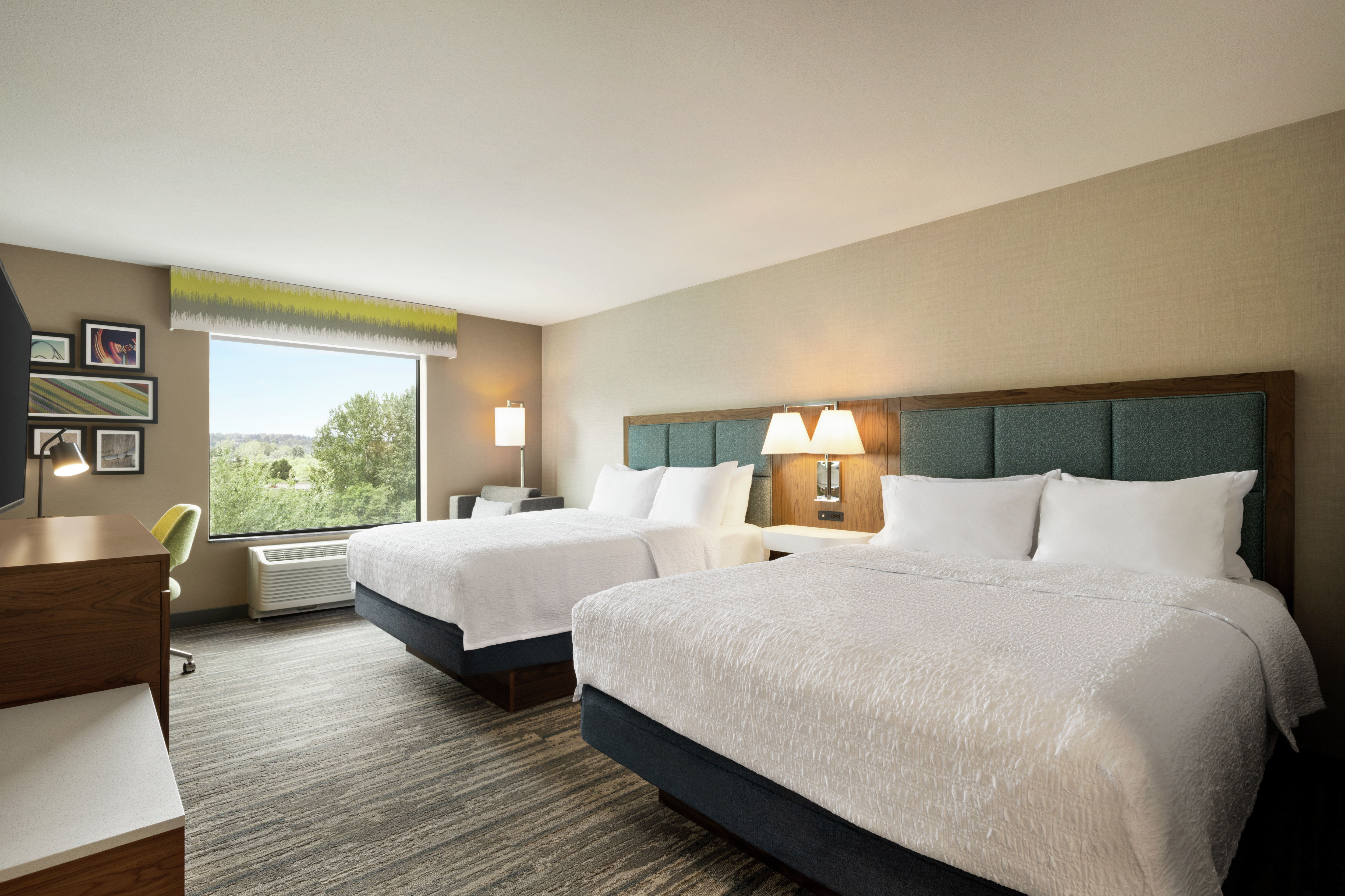 Spacious guest room featuring two comfortable queen beds, work desk, and stunning outside view.