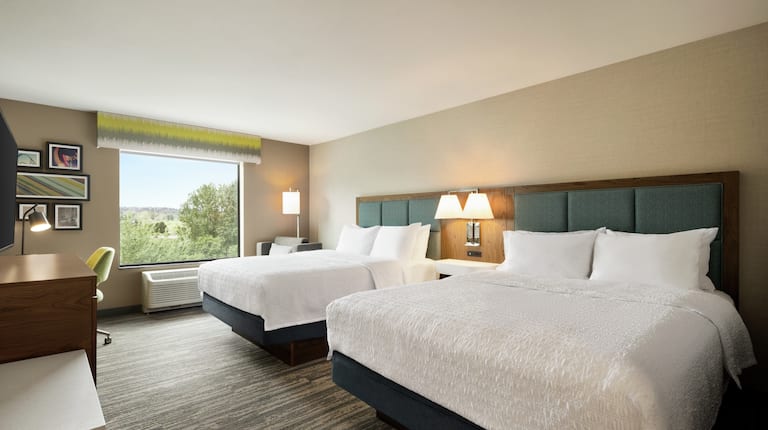 Spacious guest room featuring two comfortable queen beds, work desk, and stunning outside view.