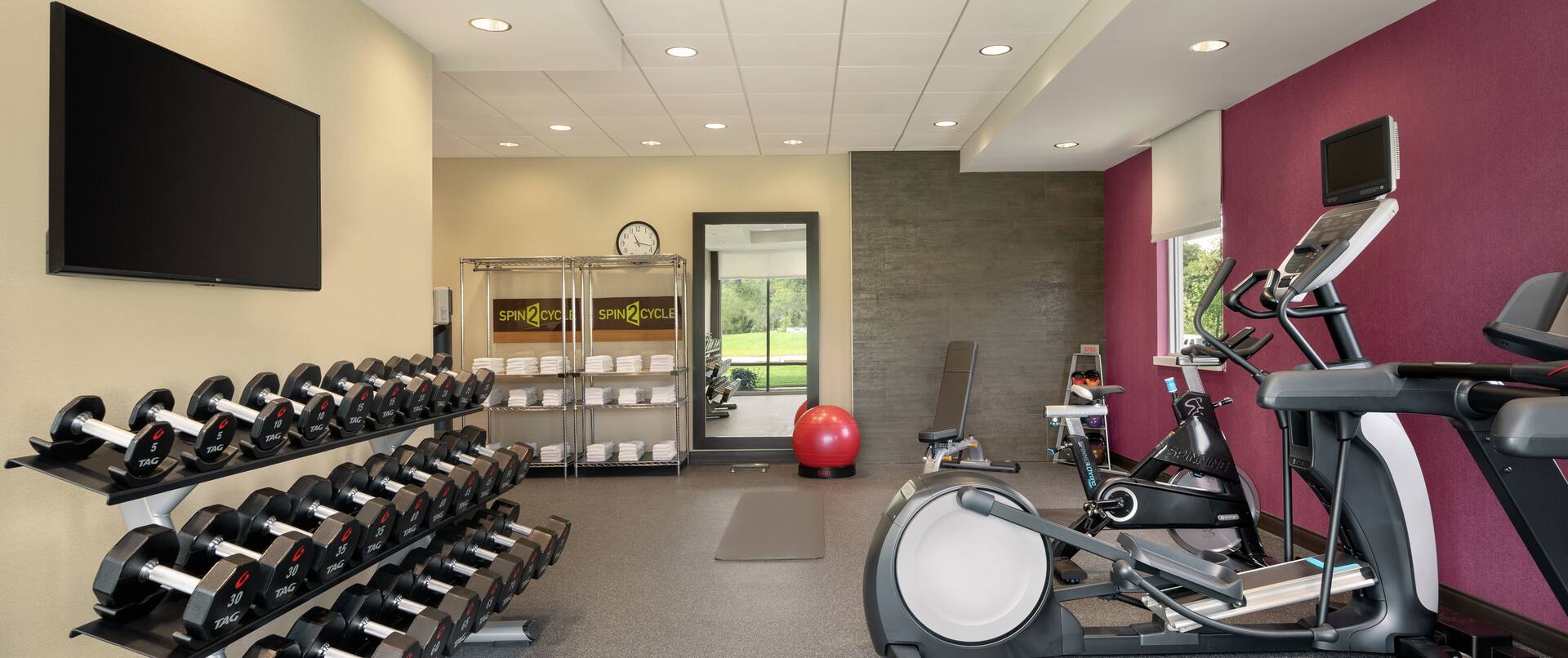 Bright fitness center featuring free weights, cardio machines, and TV.