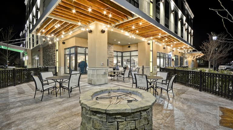 Round Fire Pit, Tables, and Chairs on Illuminated Patio at Night