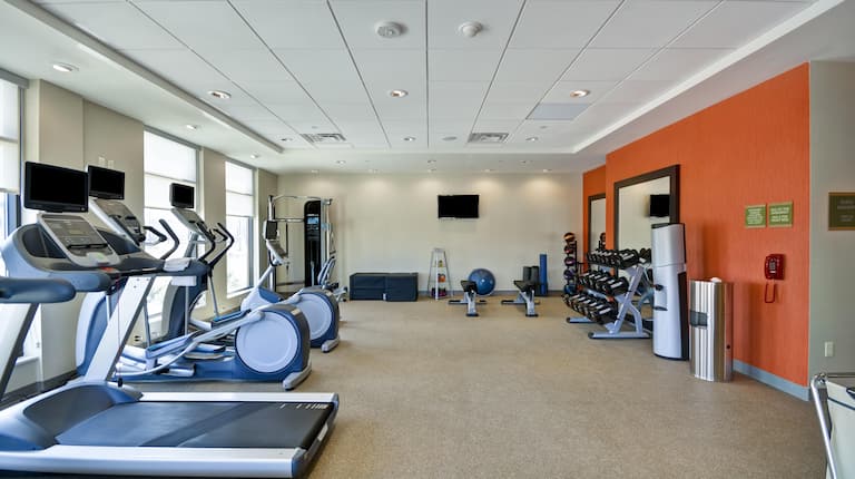 Spin2Cycle Fitness Area With Cardio Equipment Facing Windows, Weight Machine, TV, Weight Benches, Blue Exercise Ball, Weight Balls, Large Mirrors, Free Weights, and Water Cooler