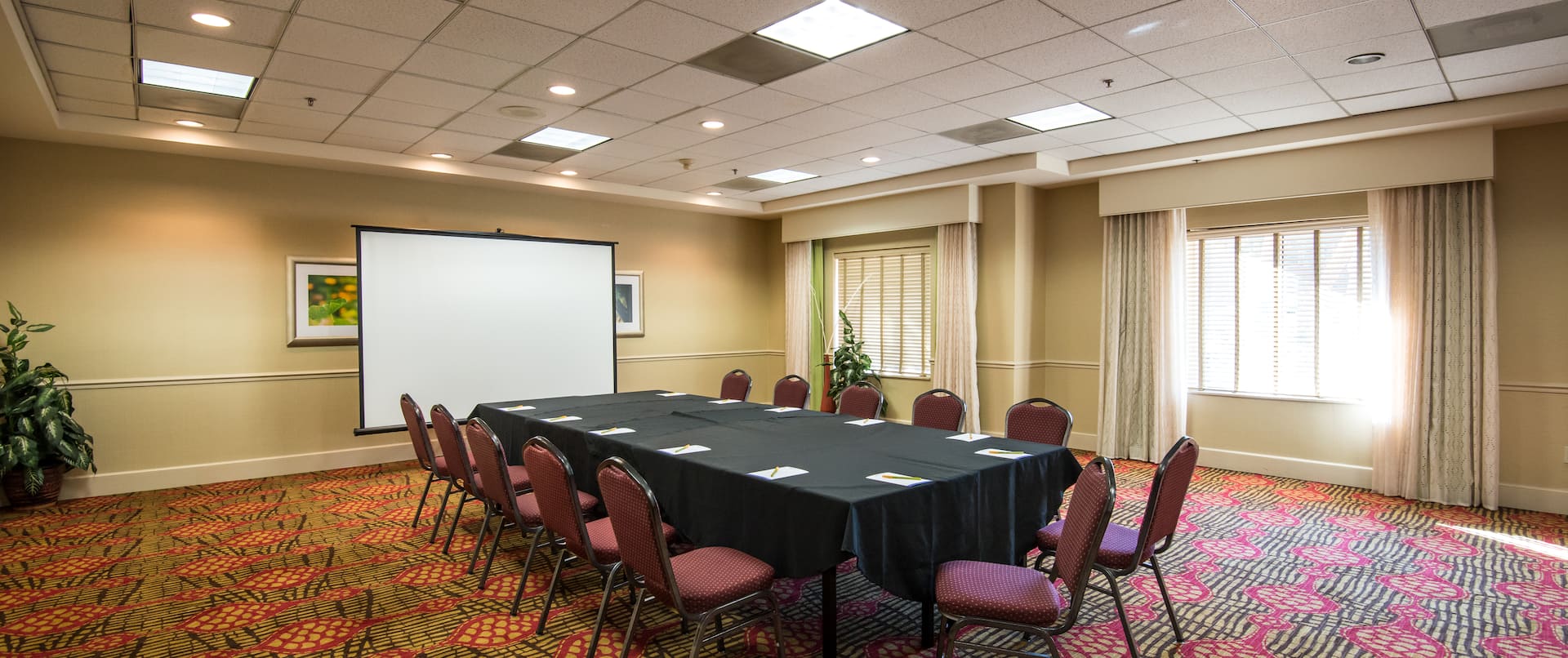 Seating for 12 at Table With Notepads on Black Linens, Presentation Screen, and Windows With Long Drapes in Meeting Room