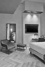 Una sedia accanto a uno specchio e un letto di fronte a una TV in una camera