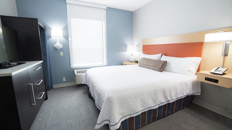 King Bed Between Two Bedside Tables With Illuminated Lamps, and TV in Studio Suite