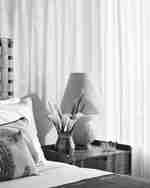 Ložnice s úhledným lůžkem, lampou a vázou na stole 