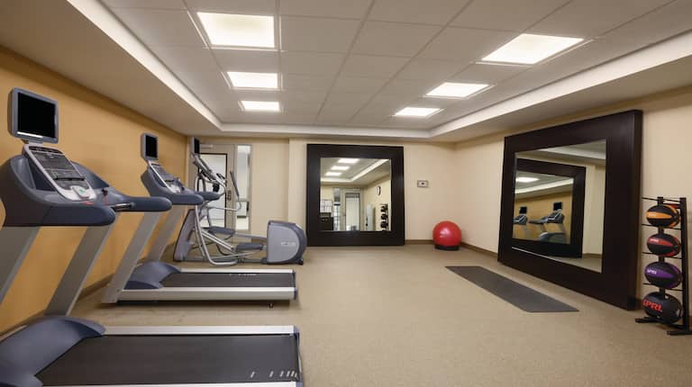Fitness Center With Cardio Equipment, Two Large Square Mirrors, Red Exercise Ball, and Weight Balls