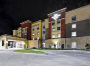 Diagonal View of Hotel Exterior, Signage, Circle Driveway, Landscaping, and Parking Lot Illuminated at Night