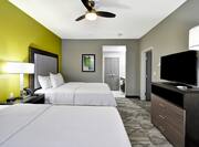 Double Queen Beds, Lamp on Bedside Table, Ceiling Fan, Wall Art, Open Doorways to Bathroom and Living Area, and TV 