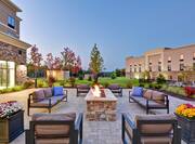 Outdoor patio space with lounge chairs and sofas surrounding fire pit, at dusk