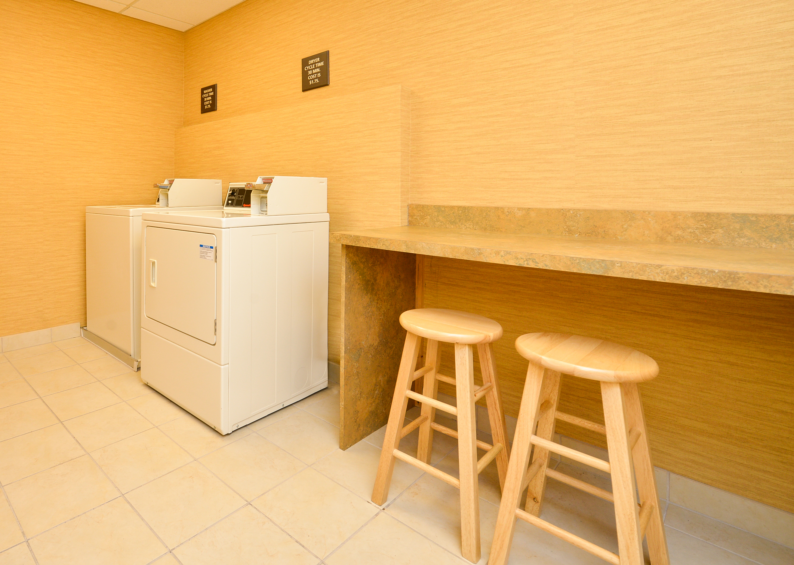 Laundry Area With Coin Operated Washing and Drying Machines, Folding Table and Two Wooden Stools