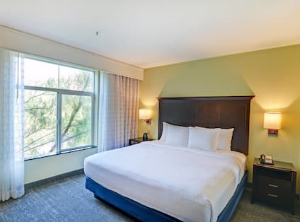 Executive suite with king bed, nightstands, wall lamps, and window with outdoor view